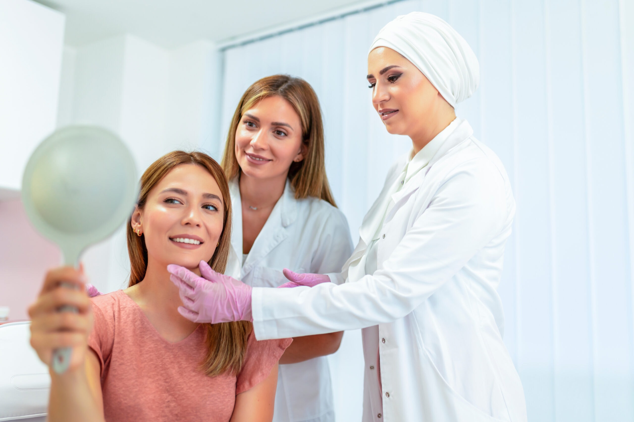 Doctor and nurse examine the patient before the aesthetic procedures. The patient is looking at herself and telling them what she wants to change.